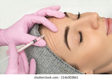 Close-up Of The Hands Of An Expert Cosmetologist Injecting Botox Into A Woman's Forehead. Correction Of Forehead And Eye Wrinkles With Botulinum Toxin.