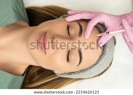 Close-up of the hands of an expert cosmetologist injecting botox into a woman's forehead. Correction of forehead and eye wrinkles with botulinum toxin.