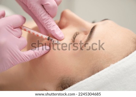 Close-up of the hands of an expert cosmetologist injecting  into a woman's forehead. Correction of forehead and eye wrinkles with botulinum toxin.