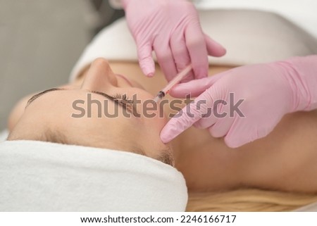 Close-up of the hands of an expert cosmetologist injecting into a woman's forehead. Correction of forehead and eye wrinkles with botulinum toxin.