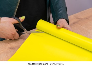 Close-up of the hands of a female florist cutting yellow wrapping paper with scissors for a bouquet in a flower shop - Powered by Shutterstock