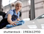 close-up hands of Female polishing the white car hood with blue rag after waxing the car for shiny look ,manual car wash and hand wash by woman in auto service. focus on hands