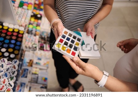 Close-up hands of a female seller, showing to a customer a beautiful palette of vibrant watercolors in creative art store. Painting. Fine art. Creativity. School stationery store. Watercolor painting