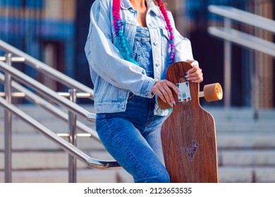 Closeup of Hands of Female Skateboarder Posing With Longboard At Fence on Stairways Outdoors While Holding Skateboard. Horizontal Image