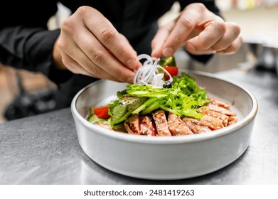 Close-up of hands garnishing a fresh salad with grilled chicken, vegetables, and greens in a white bowl. - Powered by Shutterstock