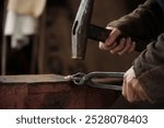 Close-up of hands hammering metal on anvil, showcasing traditional blacksmithing tools and techniques in action, highlighting craftsmanship and attention to detail