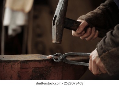 Close-up of hands hammering metal on anvil, showcasing traditional blacksmithing tools and techniques in action, highlighting craftsmanship and attention to detail - Powered by Shutterstock