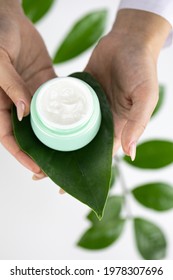 Close-up Hands Hold Cosmetic Cream Jar On Fresh Green Leaf On White Herbal Background. Skinimalism, Skincare Routines, Sustainable Packaging, Eco-conscious, Beauty, Plant-based Cosmetology Concept