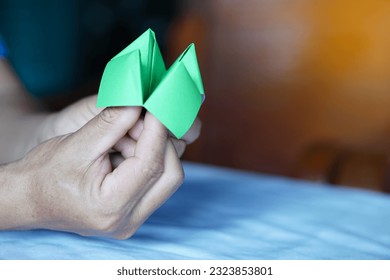 Closeup hands hold green origami paper fortune teller. Concept , Life opportunity. Paper toy that can use as creative game in summer camp or classroom activity for fun.                        