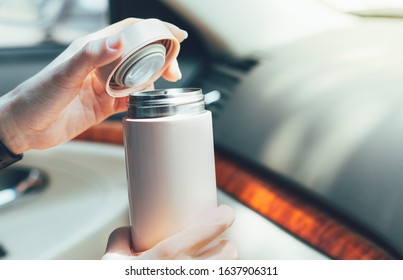 Closeup, Woman’s hands hold insulated reusable water bottle in car instead of single use plastic cup, open lid to drink her coffee. Eco friendly, zero waste and green living lifestyle.