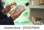 Close-up hands hold transparent bottle of body wash or shampoo. Customer reading label with ingredients, examining composition in cosmetics store, choosing cosmetic product, making purchasing decision