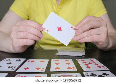 Close-up of hands holding ace of diamonds. The woman on the table is playing solitaire. Board and card games, home leisure activities. Card reading, cartomancy.
