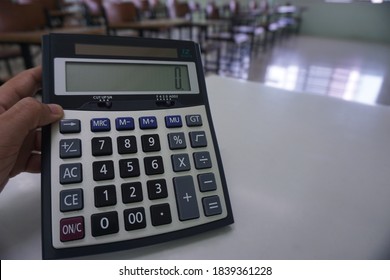 Close-up of hands holding calculator on the teacher's desk with the wood lecture chairs place distancing in the empty classroom. Back to school, business, and finance accounting concept.