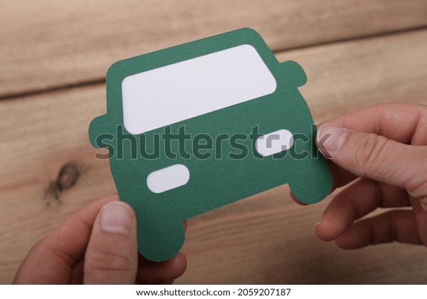 A closeup of hands holding a cardboard green car,\
above a wooden surface