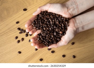 Close-up of hands holding coffee beans in a heart shape over a wooden surface.
