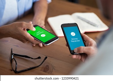 Closeup Hands Holding Mobile Phone With Application For Send And Receive Money. Man And Woman Holding Smartphone And Making Payment Transaction. Smart Phone Screen Displaying Payment Sent.