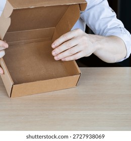 Close-up of hands holding open empty brown cardboard box over wooden table, revealing nothing inside.