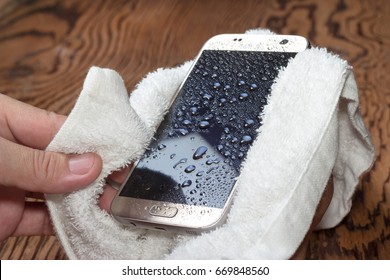closeup Hands holding White cloth with wet smart phone drops on wooden floor