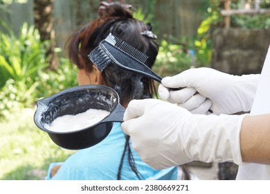 Closeup hands holds black brush to apply cream to dye hair of senior Asian woman, outdoor. Concept, Dye hair at home . Change hair color.                                - Powered by Shutterstock