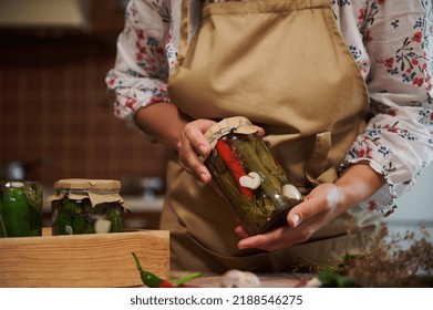 Close-up of the hands of a housewife in beige chef's apron, holding a glass jar of homemade pickled chili peppers. Marinating and preserving vegetables, healthy fermented food, winter natural products - Shutterstock ID 2188546275