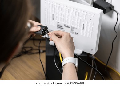 Close-up of hands inserting an Ethernet cable into a network adapter linked to a home internet router, emphasizing seamless connectivity, DIY setup, or troubleshooting