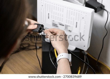 Close-up of hands inserting an Ethernet cable into a network adapter linked to a home internet router, emphasizing seamless connectivity, DIY setup, or troubleshooting