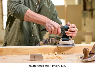 close-up hands of joiner worker using electric sander in workshop. Joiner sanding wooden board on table. Carpentery work. Small Business Concept. Copy space