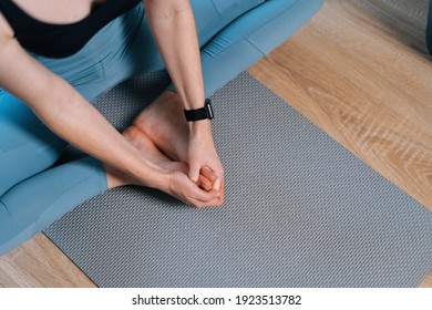 Close-up Hands And Leg Of Unrecognizable Yoga Stretching Woman On Exercise Mat At Home. Seated Butterfly Leg Stretch Holding Soles Of Feet Together With Hands, Closeup.