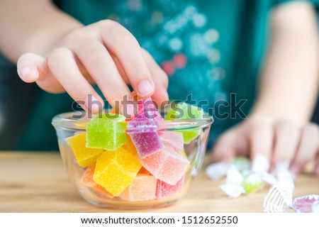 Closeup hands of a little child taking a piece of jelly cube with sugar in a glass bowl. Snacks time, Sugary treats, Party, Kids favorite, Unhealthy, Cavity, Sugar addiction, Sweetness, ADHD, Drug.