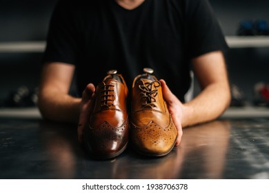 Close-up hands of male shoemaker holds old light brown leather shoe and repaired shiny shoes after restoration working. Concept of cobbler artisan repairing and restoration work in shoe repair shop. - Powered by Shutterstock