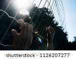 closeup of the hands of a man trying to climb up a metal fence