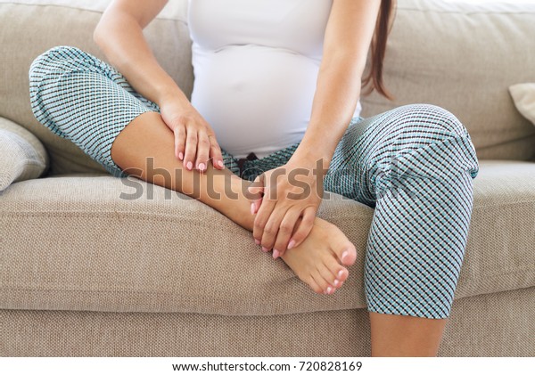 Closeup of hands massaging swollen foot while sitting on\
sofa 