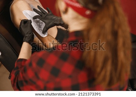Close-up hands of master in black gloves sticking paper with pattern on client hand