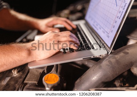 Closeup hands of mechanic with the help of diagnostic machines is ready for use with the car. Laptop torque figures and horsepower is the engine of the vehicle for diagnostics and configuration.