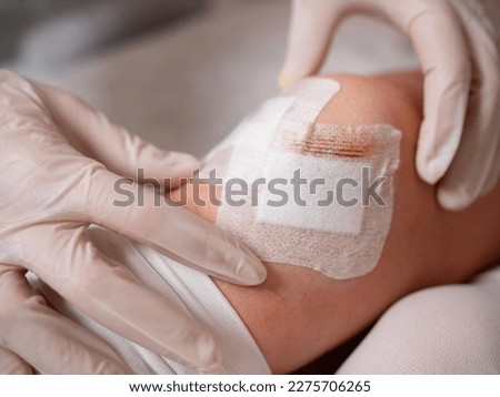Close-up of the hands of a nurse in sterile gloves at the knee of a patient sticking a sterile patch during dressing after arthroscopy surgery.