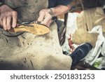 Close-up of the hands of an old master shoemaker in a leather apron using pliers to repair a shoe. In his messy workshop. Concept: Shoe repair circular economy and ecology against planned obsolescence