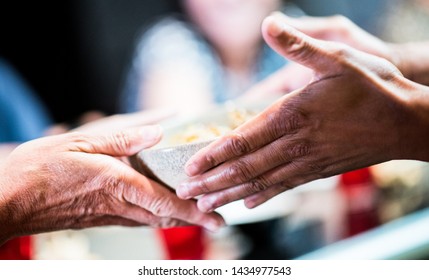 Closeup of hands of older tanned white Caucasian woman taking a bowl of food from dark skin African young male chef from Cape Verde islands. Culture, age, ethnic diversity, love and caring concepts