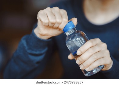 Close-up of hands opening a small plastic water bottle. Concept of hydration, daily water intake, and healthy lifestyle in everyday life. - Powered by Shutterstock