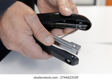 Close-up of hands opening a stapler to insert or check staples during office work. Concept for maintenance, office supplies, preparation, and workplace tools
