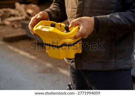 Close-up of hands operating a yellow remote control for an overhead crane system in an industrial steel warehouse environment.