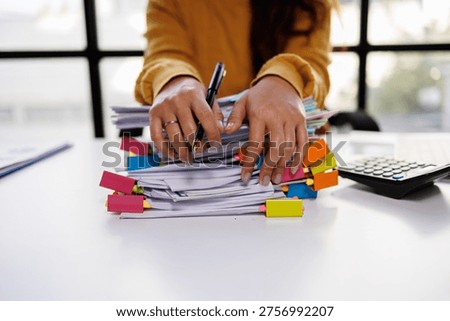 Close-up of hands organizing a colorful stack of documents with tabs, highlighting the tactile engagement with the task in a contemporary office setting equipped with essential tools.