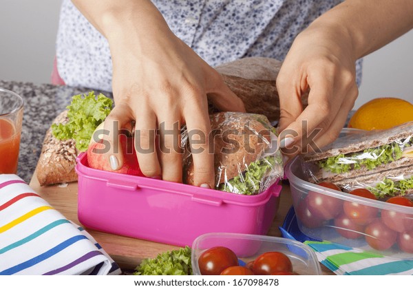 A\
closeup of hands packing snacks into a pink lunch\
box