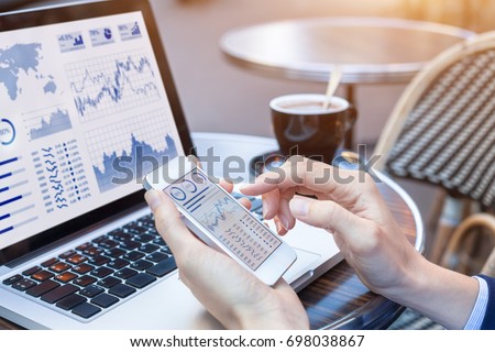 Close-up of hands of person analyzing stock market chart and key performance indicators (KPI) with business intelligence (BI) on notebook computer and smartphone screen, fintech (financial technology)