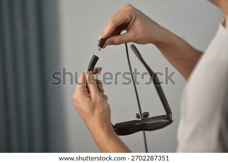 Close-up of hands plugging a USB-C cable into smart AR glasses. Concept of modern tech, wearable devices, charging, connectivity, and digital lifestyle.