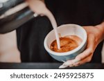 Close-up of a barista’s hands pouring milk from a metal pitcher into a blue coffee cup, creating intricate latte art. The scene captures the precision and artistry involved in making specialty coffee