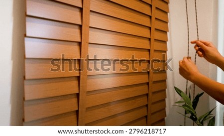 Close-up of hands pulling a beaded cord to adjust horizontal wooden window blinds.
