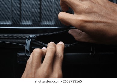 A close-up of hands pulling open a black zipper on a textured suitcase, focusing on the detail of the luggage closure. Travel and accessibility