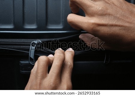 A close-up of hands pulling open a black zipper on a textured suitcase, focusing on the detail of the luggage closure. Travel and accessibility