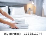 Close-up of hands putting stack of fresh white bath towels on the bed sheet. Room service maid cleaning hotel room.