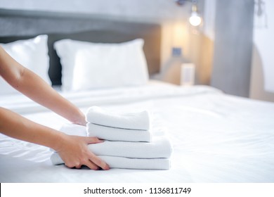Close-up of hands putting stack of fresh white bath towels on the bed sheet. Room service maid cleaning hotel room. - Shutterstock ID 1136811749